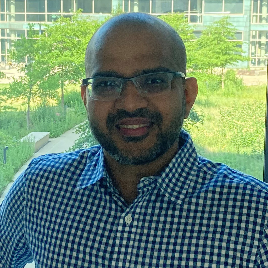 man in blue/white checked shirt, smiling, looking at camera